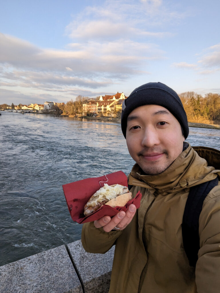 Me eating a historic bratwurst on the old stone bridge in Regensburg, Germany, photo by Alex Lau